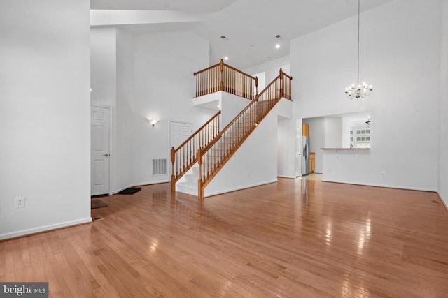 unfurnished living room featuring ceiling fan with notable chandelier, a towering ceiling, and light wood-type flooring