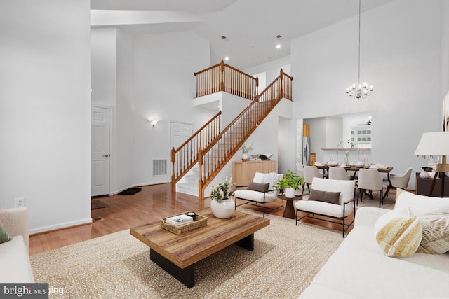 living room featuring wood-type flooring, ceiling fan with notable chandelier, and a high ceiling