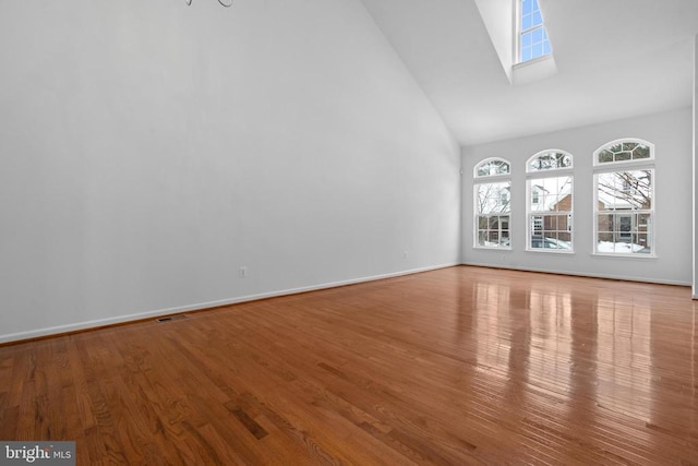 empty room featuring hardwood / wood-style flooring, high vaulted ceiling, and a skylight