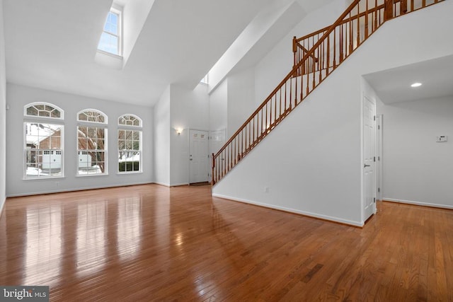 unfurnished living room featuring a high ceiling, wood-type flooring, and a skylight