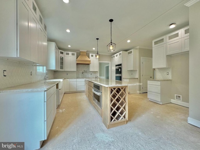 kitchen featuring custom exhaust hood, hanging light fixtures, a center island with sink, white cabinetry, and stainless steel double oven