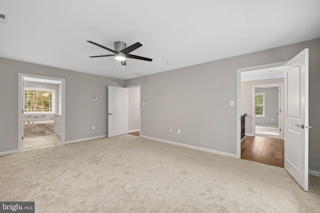 unfurnished bedroom featuring connected bathroom, ceiling fan, light carpet, and multiple windows