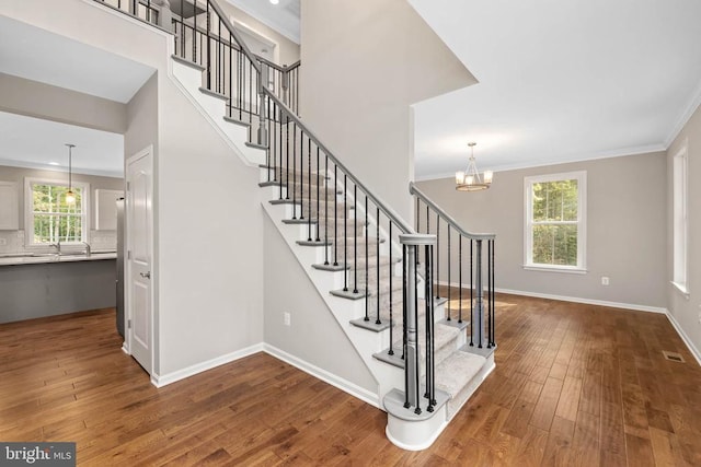 staircase with hardwood / wood-style floors, a chandelier, ornamental molding, and plenty of natural light