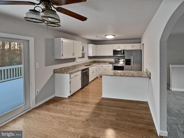 kitchen featuring dark stone countertops, appliances with stainless steel finishes, light wood-type flooring, sink, and white cabinetry