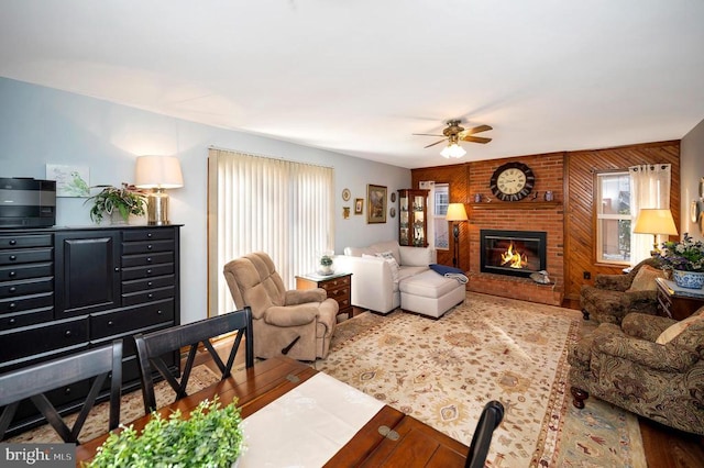 living room featuring wood-type flooring, wooden walls, a brick fireplace, and ceiling fan