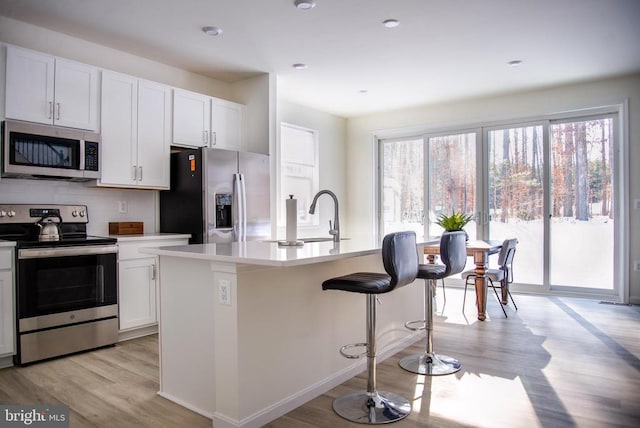 kitchen with stainless steel appliances, sink, white cabinets, and a kitchen island with sink