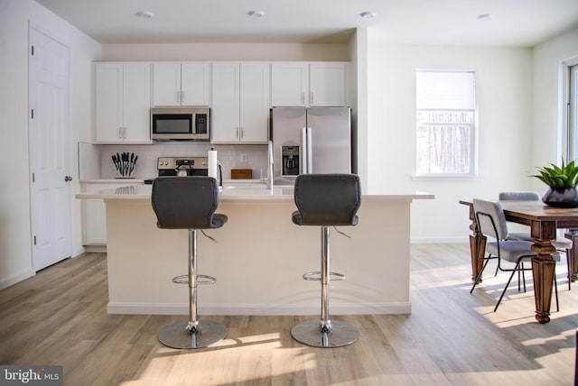 kitchen with white cabinets, appliances with stainless steel finishes, a kitchen bar, backsplash, and a center island with sink