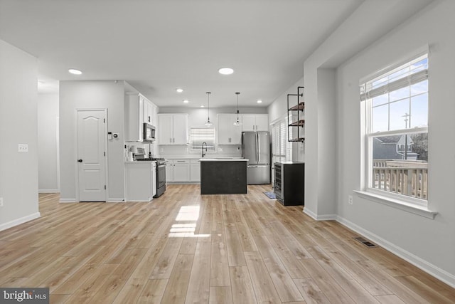 kitchen with white cabinetry, light hardwood / wood-style flooring, appliances with stainless steel finishes, a kitchen island, and pendant lighting