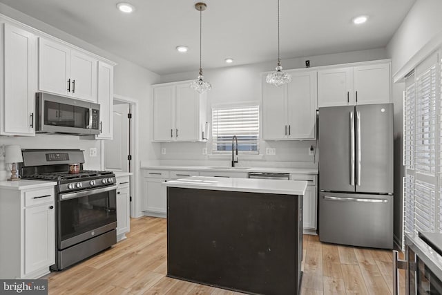 kitchen with appliances with stainless steel finishes, pendant lighting, white cabinetry, sink, and light wood-type flooring