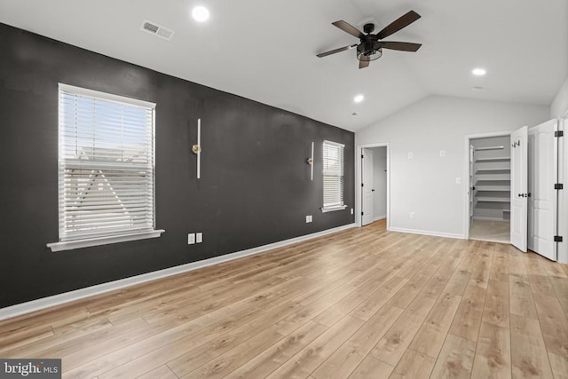 unfurnished bedroom featuring ceiling fan, vaulted ceiling, light hardwood / wood-style flooring, and a walk in closet