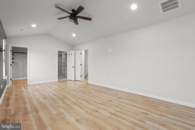 unfurnished bedroom featuring lofted ceiling, a spacious closet, light wood-type flooring, a closet, and ceiling fan