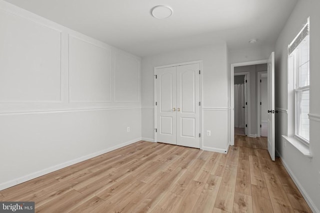 unfurnished bedroom with multiple windows, a closet, and light wood-type flooring