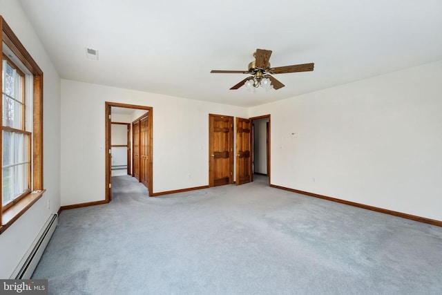 unfurnished bedroom featuring light carpet, ceiling fan, a baseboard radiator, a closet, and a walk in closet