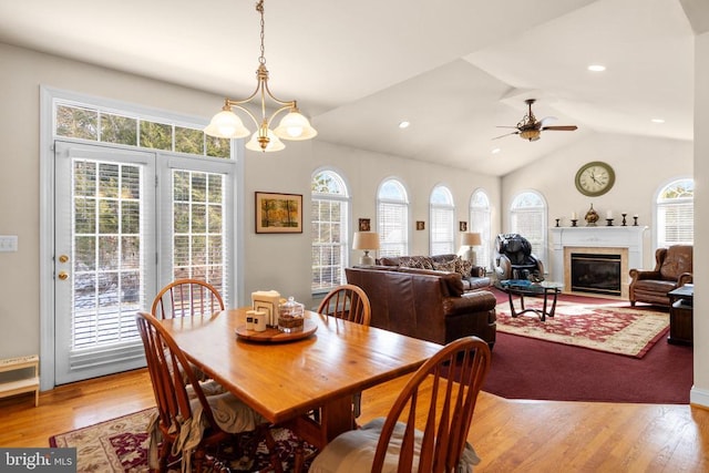 dining room with vaulted ceiling, ceiling fan with notable chandelier, and light hardwood / wood-style floors