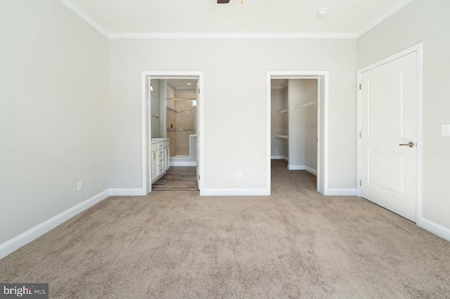 unfurnished bedroom with ensuite bathroom, light colored carpet, crown molding, a walk in closet, and a closet