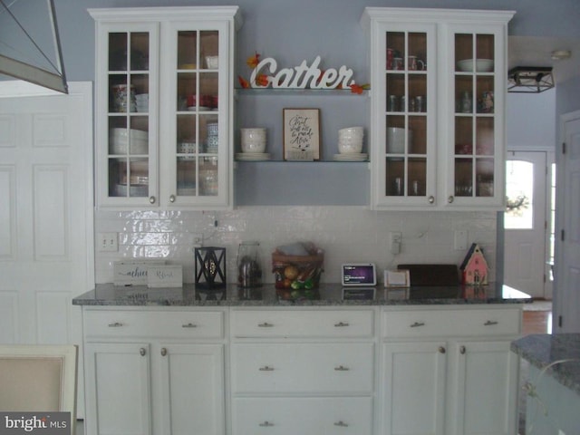 bar with white cabinetry, backsplash, and dark stone counters