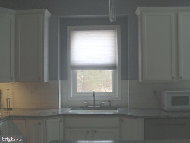 kitchen with backsplash, light stone countertops, sink, and white cabinets