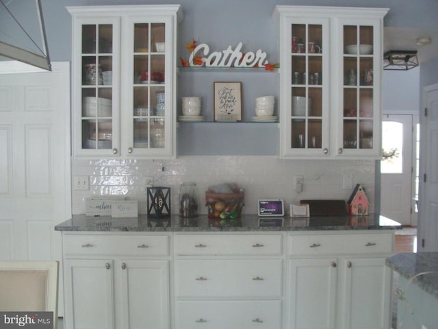 bar with dark stone countertops, decorative backsplash, and white cabinets