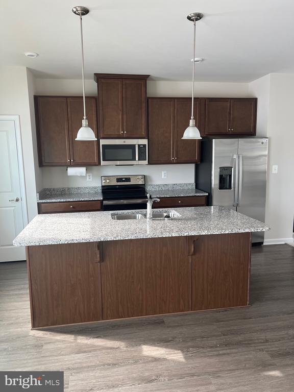 kitchen featuring dark wood-type flooring, light stone countertops, an island with sink, and appliances with stainless steel finishes