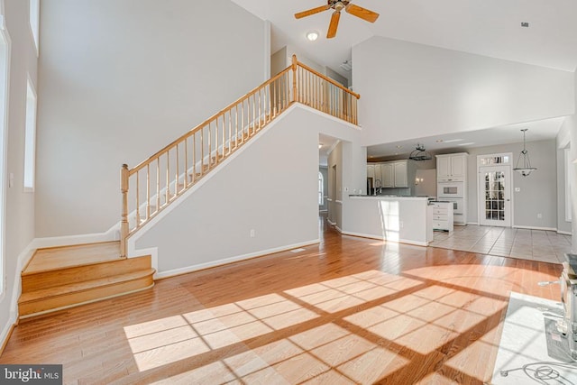 unfurnished living room featuring high vaulted ceiling, a healthy amount of sunlight, and light wood-type flooring