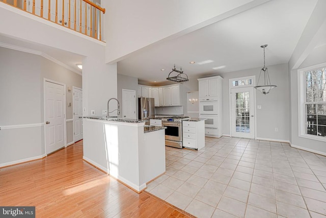 kitchen featuring appliances with stainless steel finishes, a towering ceiling, pendant lighting, white cabinets, and light hardwood / wood-style flooring