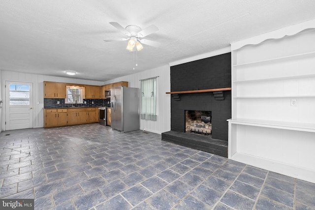 unfurnished living room with ceiling fan, a brick fireplace, sink, and a textured ceiling