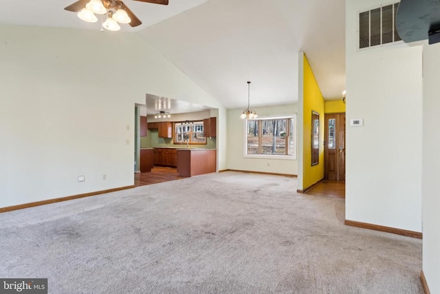 unfurnished living room featuring ceiling fan with notable chandelier, light carpet, and high vaulted ceiling