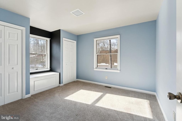 unfurnished bedroom featuring multiple windows, multiple closets, and carpet flooring