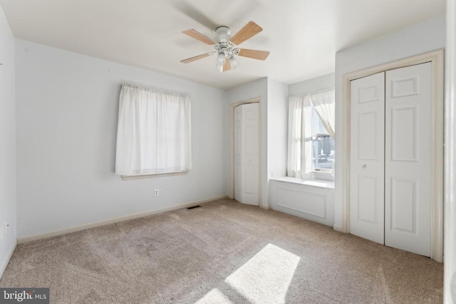 unfurnished bedroom with light carpet, two closets, and ceiling fan