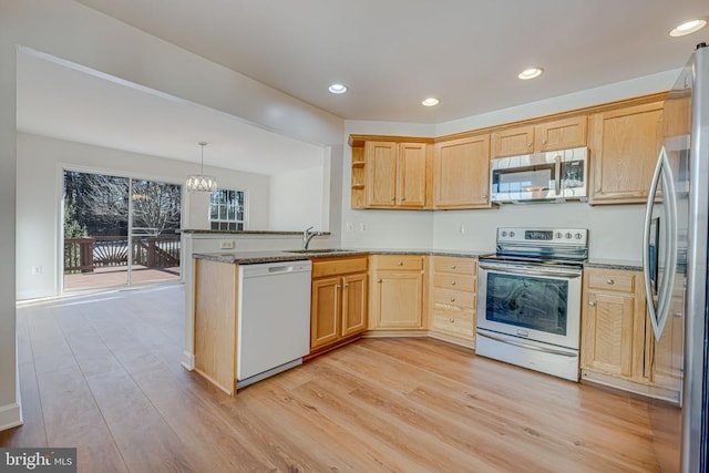 kitchen with sink, appliances with stainless steel finishes, kitchen peninsula, pendant lighting, and light hardwood / wood-style floors