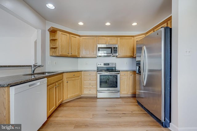 kitchen with appliances with stainless steel finishes, sink, dark stone countertops, light hardwood / wood-style floors, and kitchen peninsula