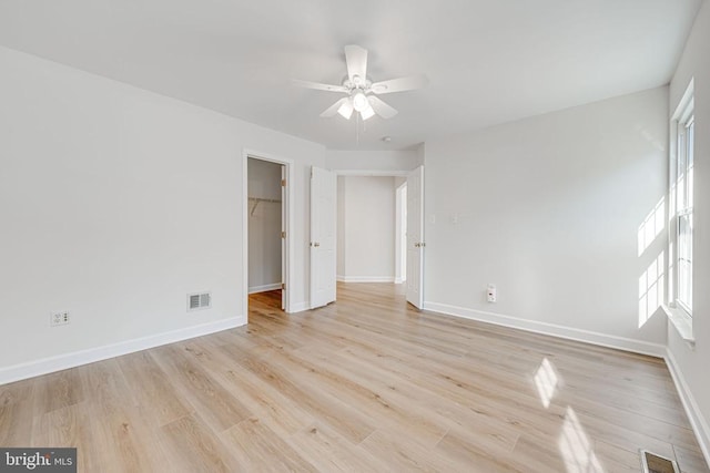 unfurnished bedroom with a spacious closet, light hardwood / wood-style flooring, a closet, and ceiling fan