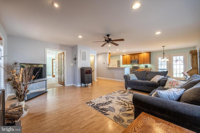 living room with ceiling fan with notable chandelier and light hardwood / wood-style flooring