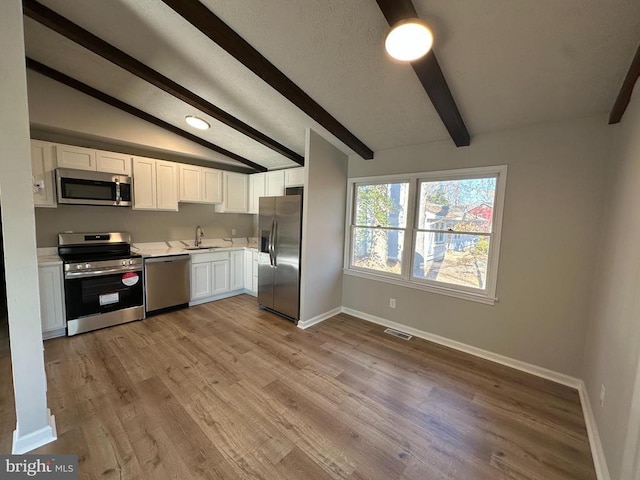 kitchen featuring lofted ceiling with beams, white cabinetry, sink, stainless steel appliances, and light hardwood / wood-style flooring