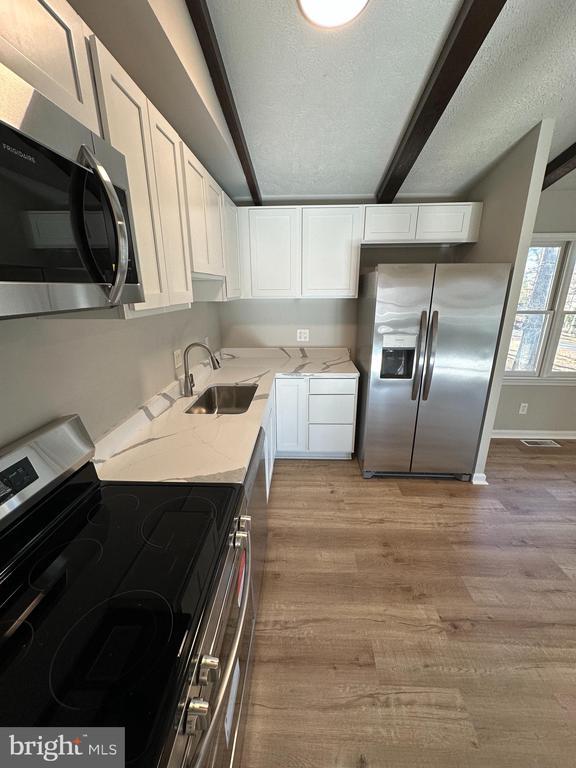 kitchen featuring sink, white cabinetry, light stone counters, lofted ceiling with beams, and appliances with stainless steel finishes