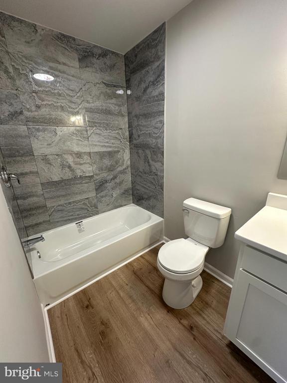 full bathroom with vanity, hardwood / wood-style floors, tiled shower / bath combo, and toilet