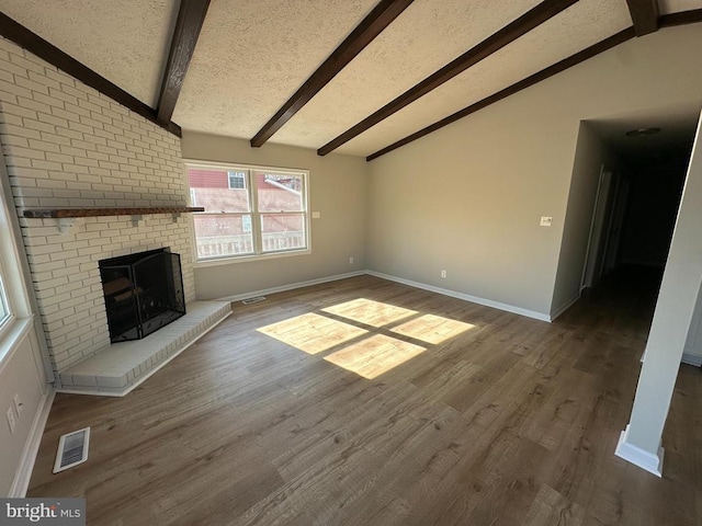 unfurnished living room with wood-type flooring, a fireplace, lofted ceiling with beams, and a textured ceiling