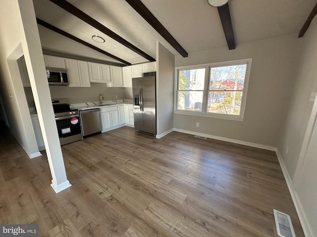 kitchen with sink, white cabinetry, lofted ceiling with beams, stainless steel appliances, and light hardwood / wood-style floors