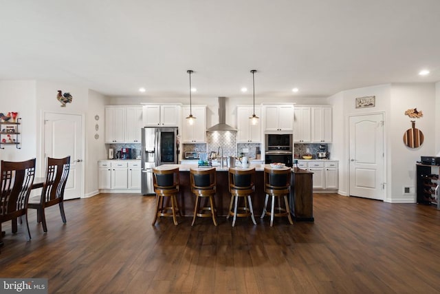 kitchen featuring white cabinetry, decorative light fixtures, an island with sink, and wall chimney exhaust hood