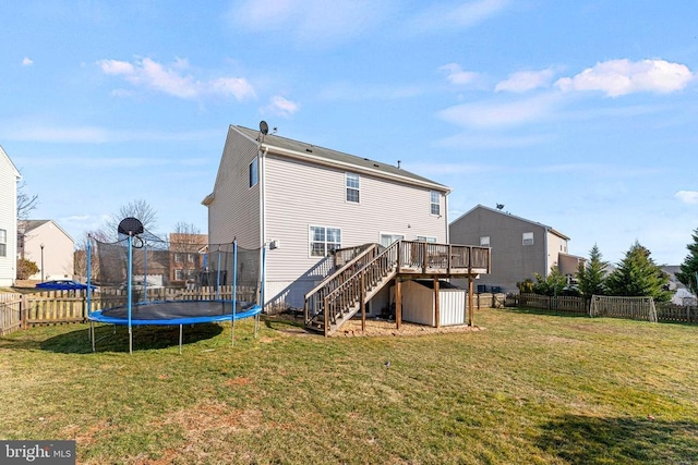 back of house with a wooden deck, a trampoline, and a lawn