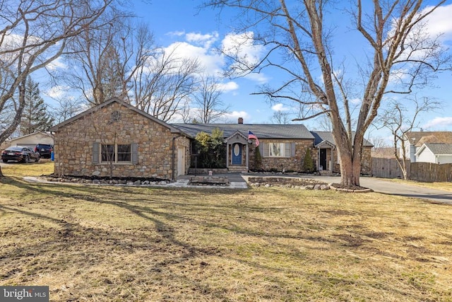 single story home featuring stone siding, a chimney, a front yard, and fence