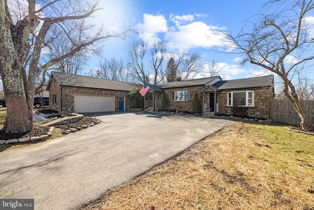 view of front of home featuring aphalt driveway, stone siding, a garage, and fence