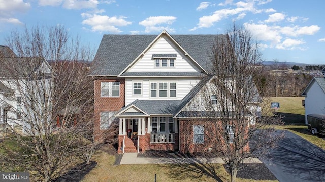 view of front of property with brick siding, a porch, a front lawn, and a shingled roof