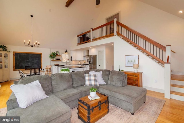 living area with a chandelier, high vaulted ceiling, baseboards, stairs, and light wood finished floors