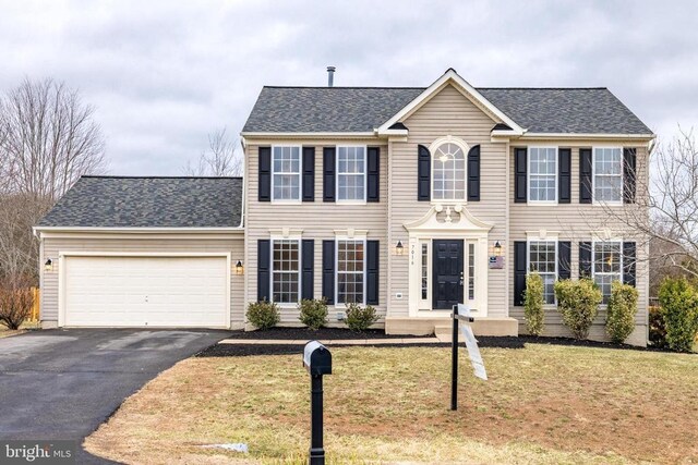 colonial home featuring an attached garage, a shingled roof, aphalt driveway, and a front yard