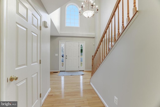 foyer featuring a chandelier, a towering ceiling, baseboards, stairs, and light wood finished floors