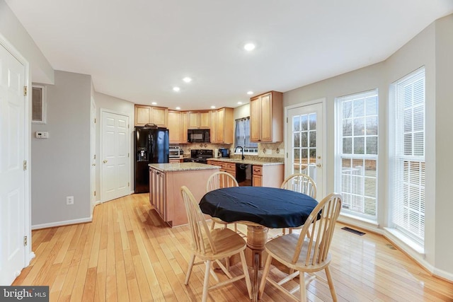 kitchen featuring light brown cabinets, light wood-style flooring, a kitchen island, backsplash, and black appliances