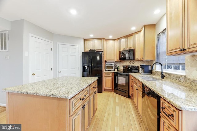 kitchen with light wood finished floors, light stone counters, a sink, black appliances, and backsplash