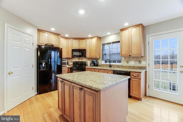 kitchen with tasteful backsplash, light wood-style flooring, light stone counters, black appliances, and a sink