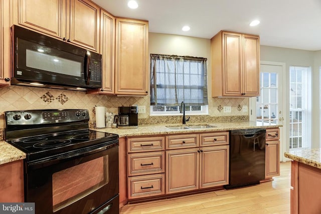 kitchen with a healthy amount of sunlight, black appliances, a sink, and light stone countertops